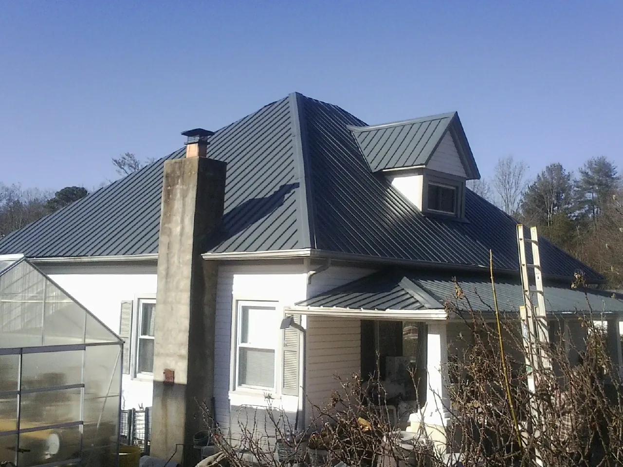 Dark blue standing seam metal roof on a white farmhouse with dormer — Slate & Tile Roof Repair by Roofing Brothers in Charlotte Court House