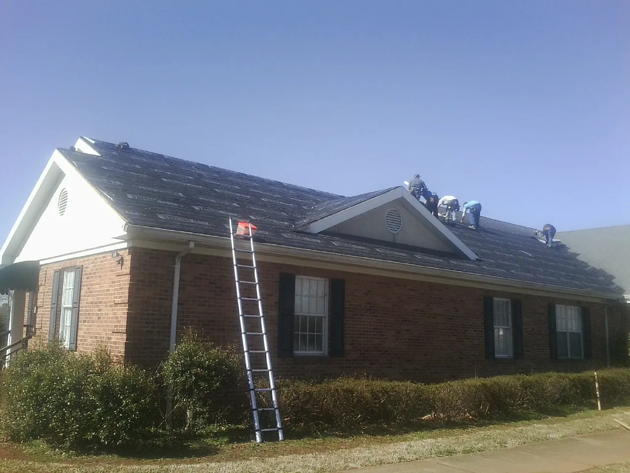 Crew tearing shingles off a brick ranch roof with a ladder set — Emergency Roof Repair work by our crew in Charlotte Court House