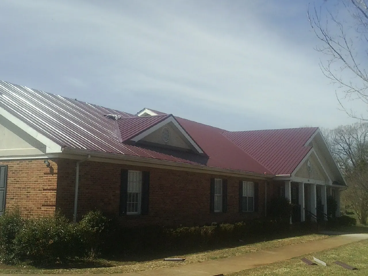 Red metal roof with gabled entries on a long brick building, from a Hail Damage Roof Repair job in Charlotte Court House