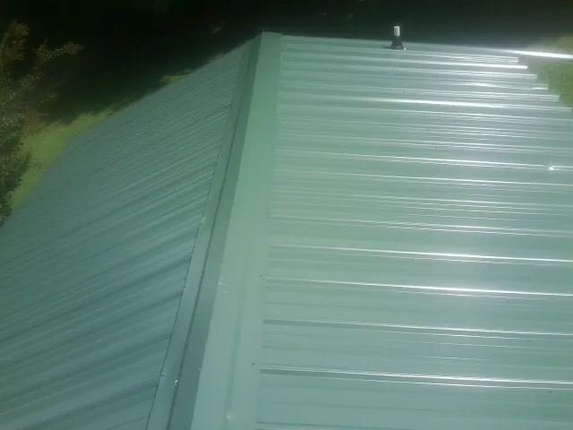 New green metal panels meeting at the ridge of a roof — Flat Roof Repair work by our crew in Charlotte Court House