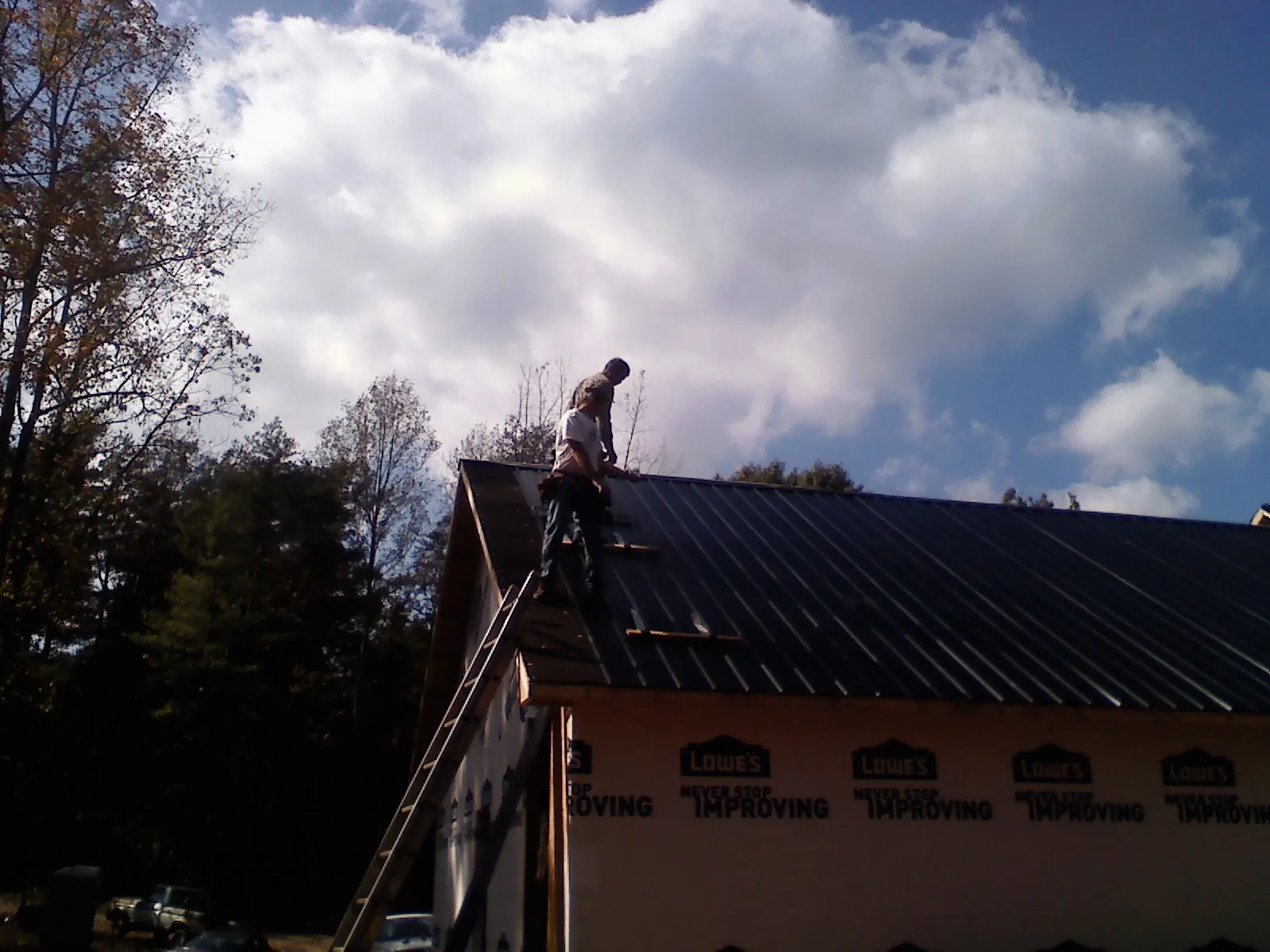 Roofer fastening dark metal panels high against a cloudy sky, from a Roof Inspection job in Charlotte Court House