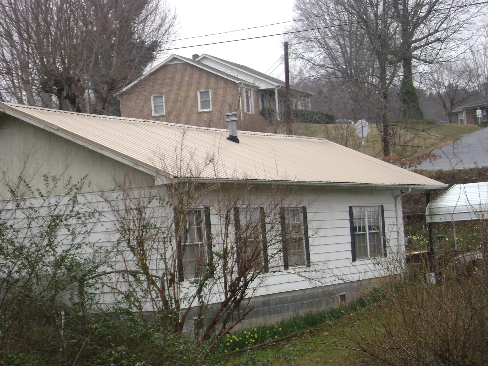 Tan metal roof on a white sided house set into a hillside — Commercial Roofing by Roofing Brothers in Charlotte Court House
