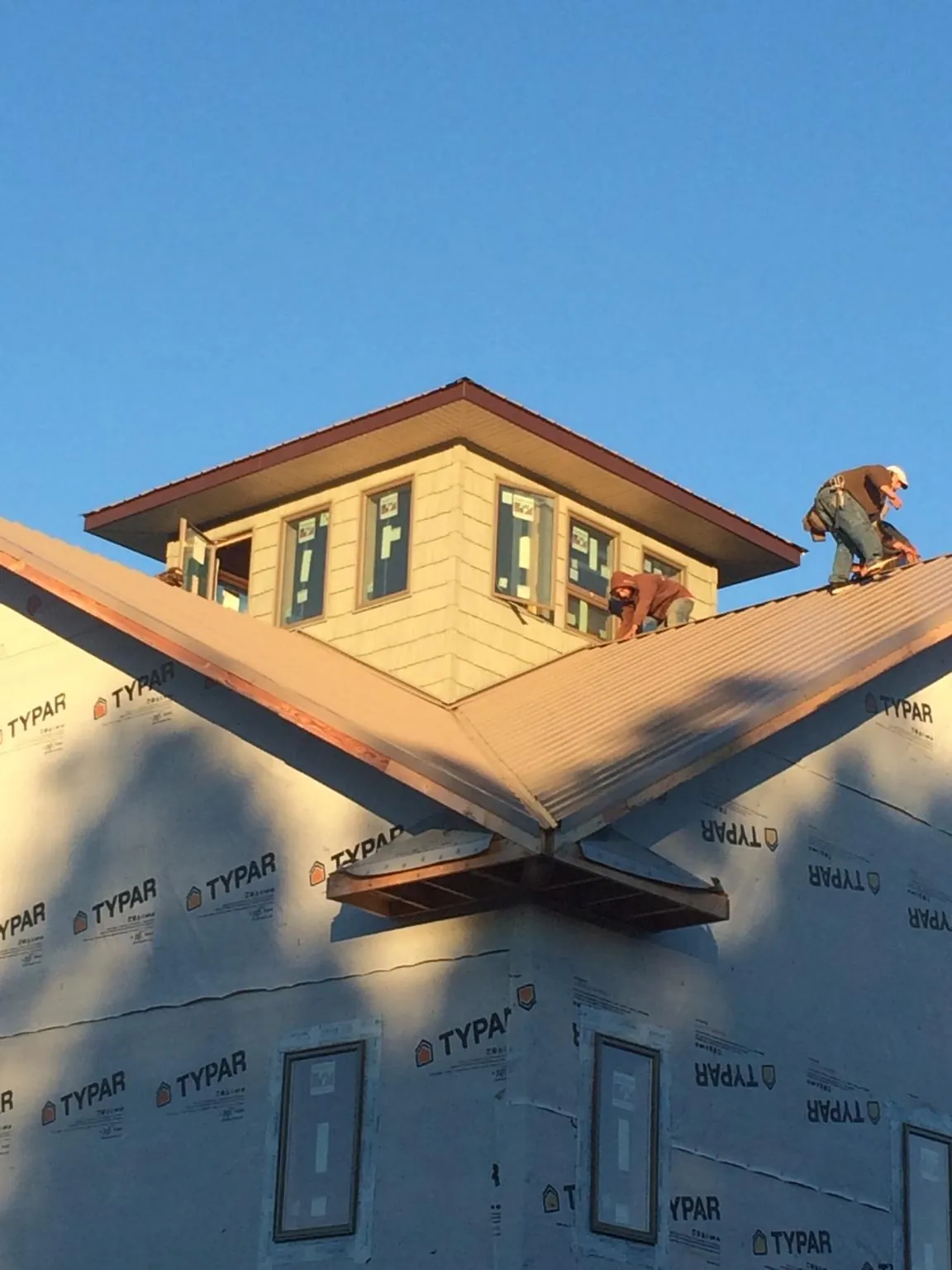 Roofers working around a rooftop cupola on a new metal roof at sunset — Roof Waterproofing in Charlotte Court House by Roofing Brothers